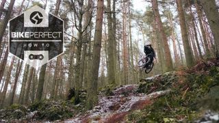 A rider jumps off a rock drop in a forest and adds some style by turning the handlebars 