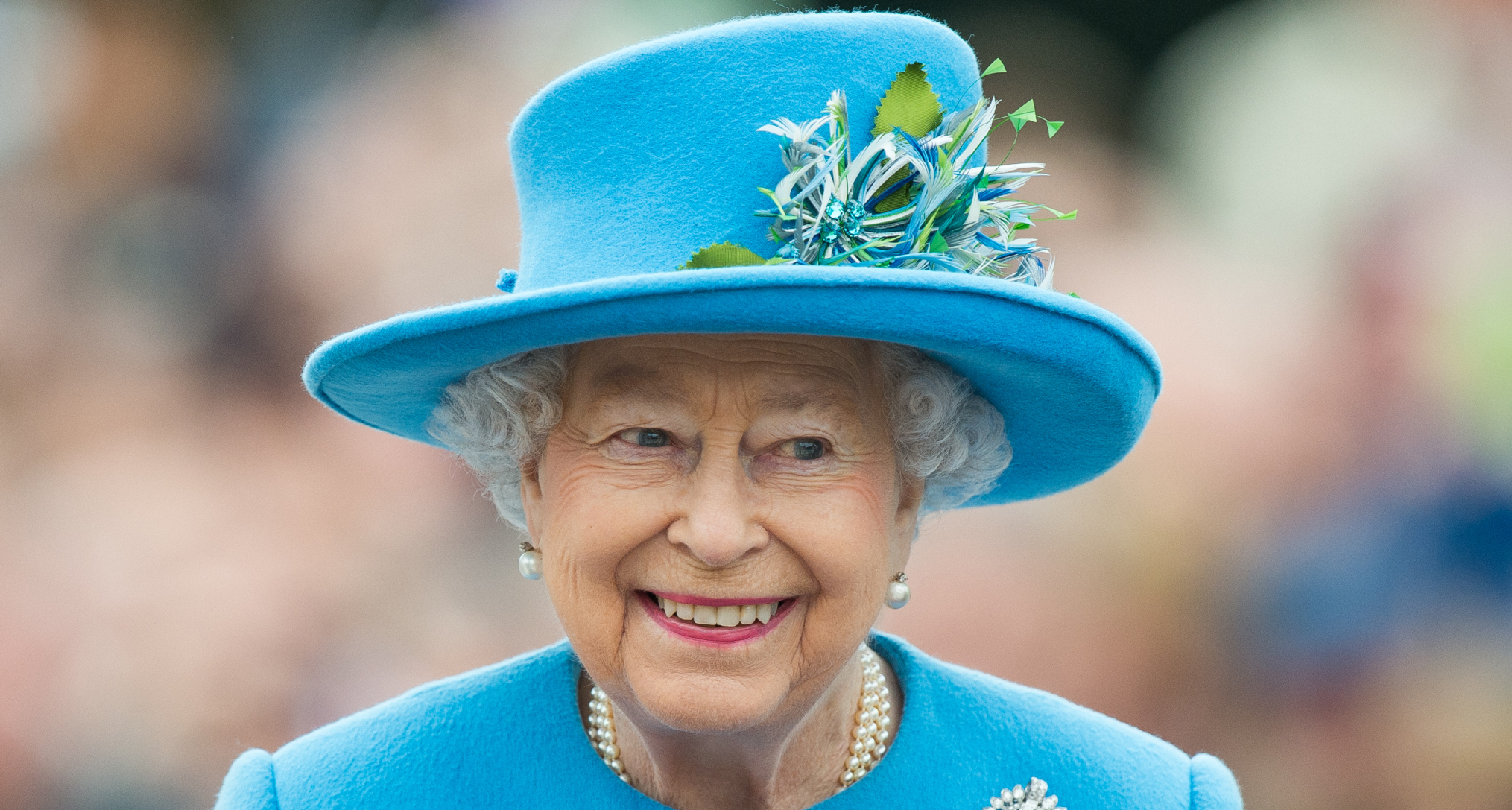 Queen Elizabeth wearing a turquoise hat and coat and smiling