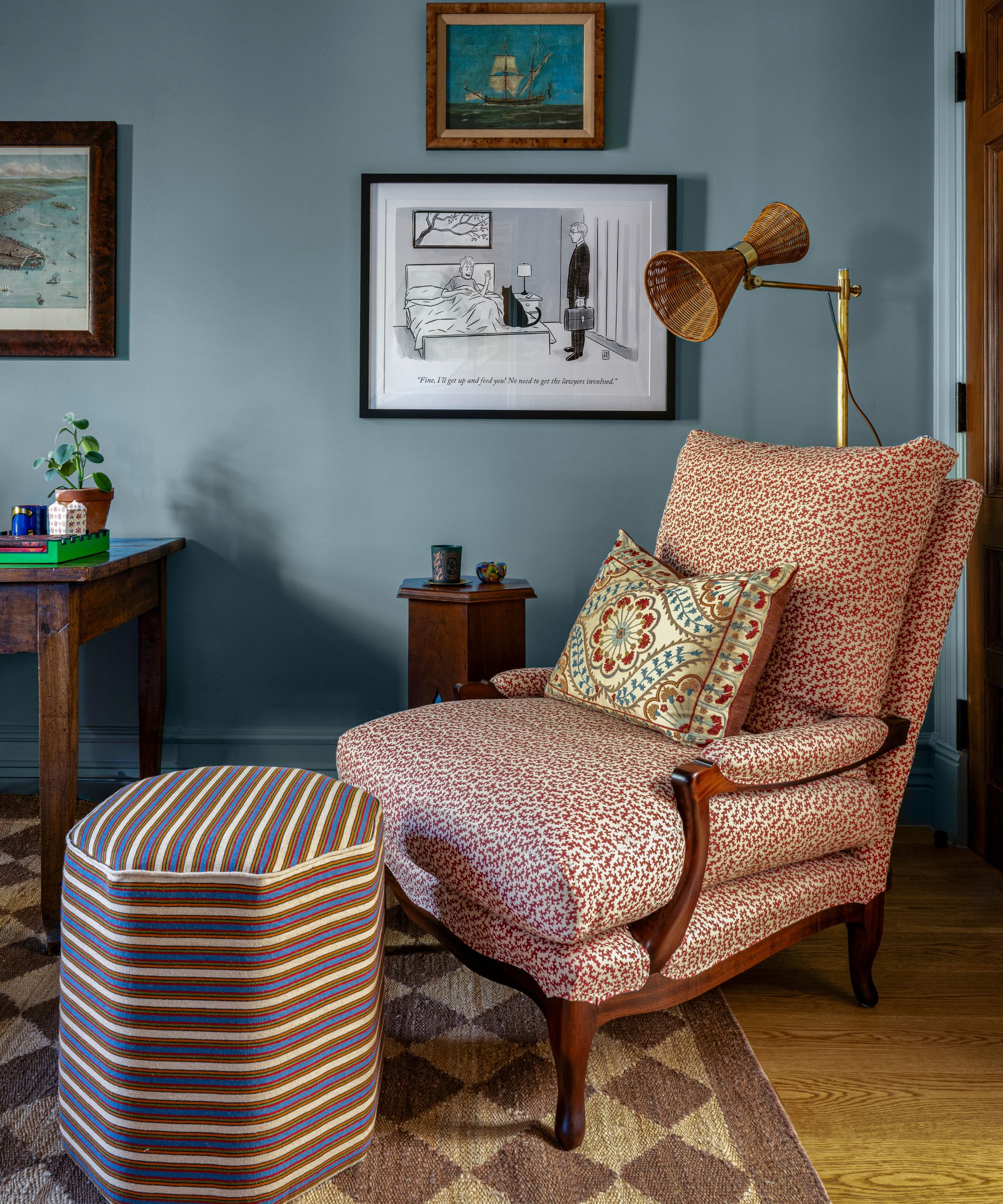 a blue painted home office with antique desk, a floral vintage chair, striped ottoman and vintage artwork