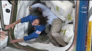 A NASA astronaut in blue reaches her hand to a crewmate as she enters space station