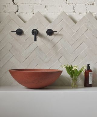 A bathroom backsplash idea with rectangular taupe tiles in a herringbone layout