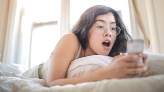 Woman on bed looking at smartphone in surprise