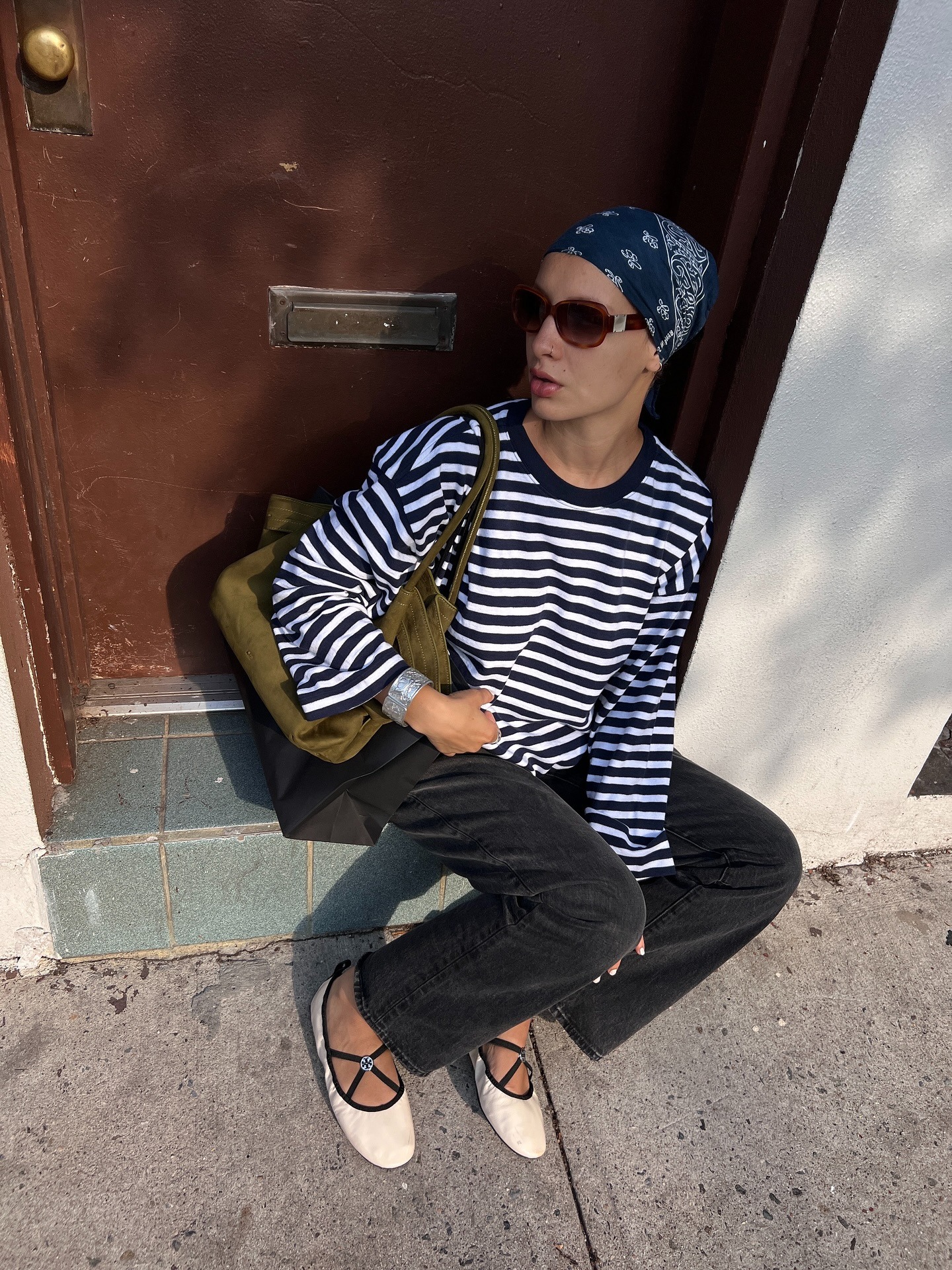 Aisha Farida wearing a striped black and white longsleeve shirt, black jeans, a green shoulder bag, and satin white flats
