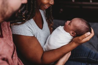 Parents smiling at multiracial infant swaddled in white blanket