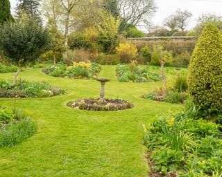 A sundial set within a stone lined circular bed surrounded by island beds in a spring garden