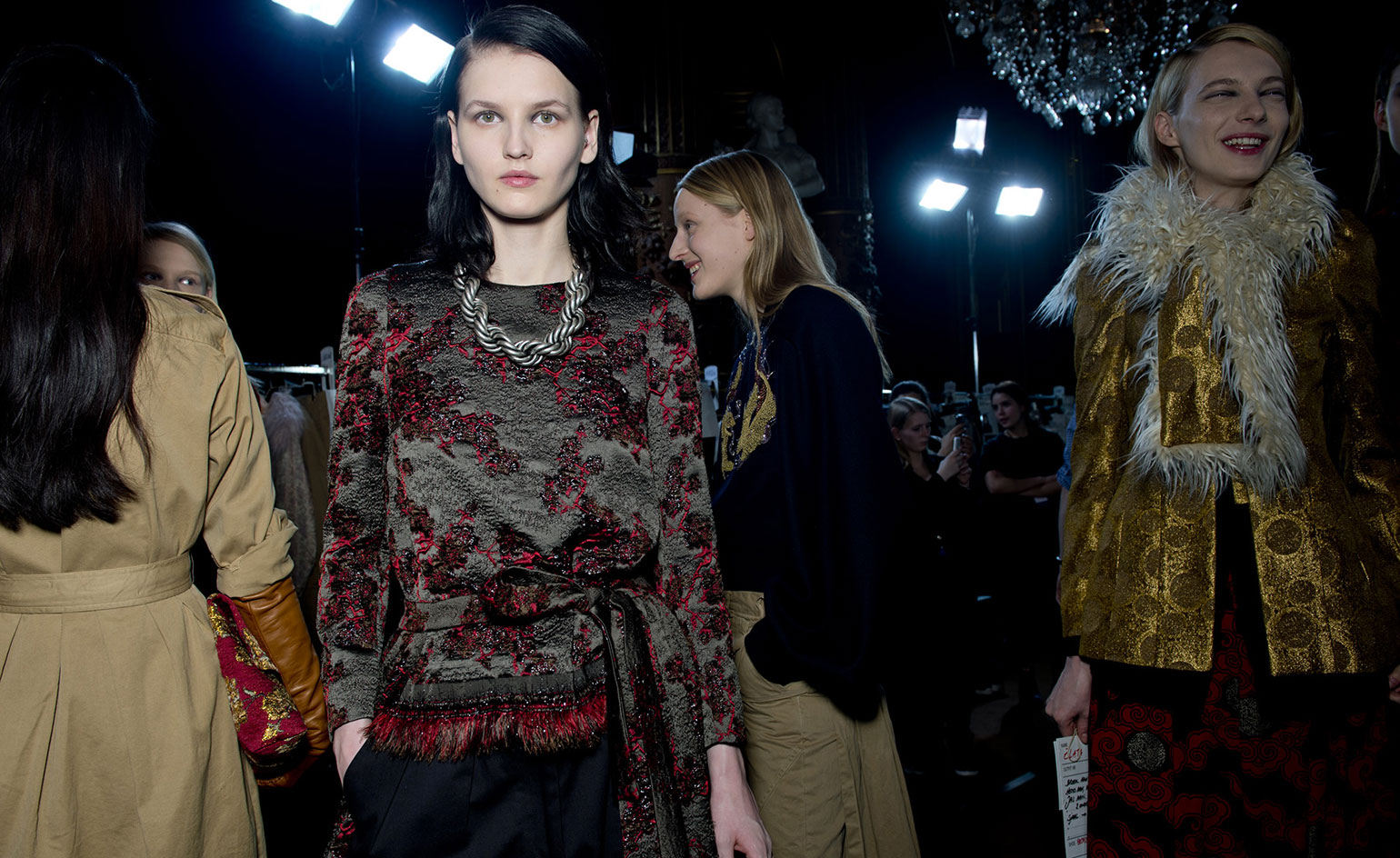 Woman wearing a black satin top with black and red embroidered detailing. People in the background