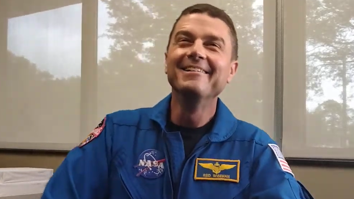 commander reid wiseman smiling in his flight suit in an office