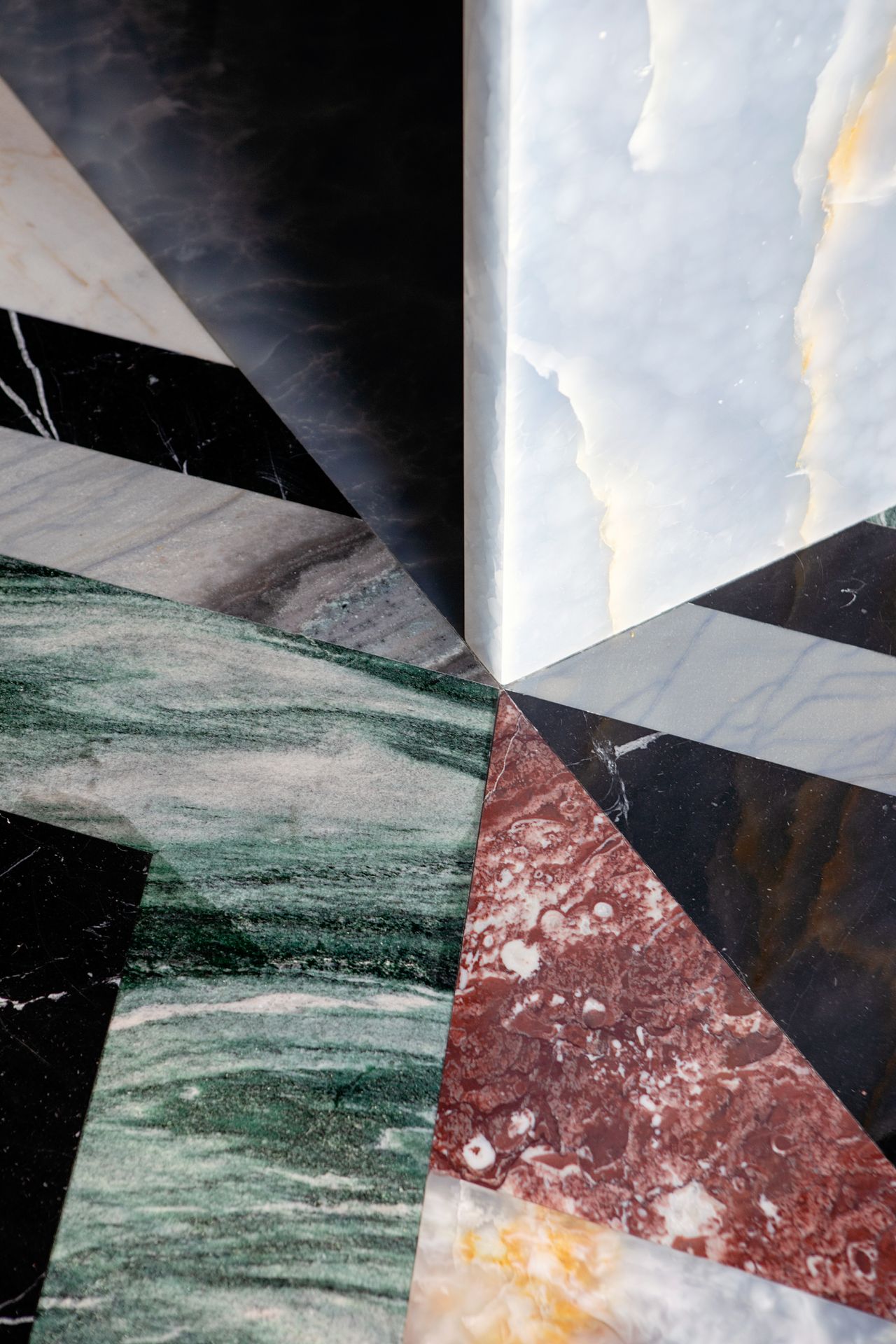 Close-up image of a floor that is made of multiple types of marble. The colors are an emerald green, a brick red, and black and white.