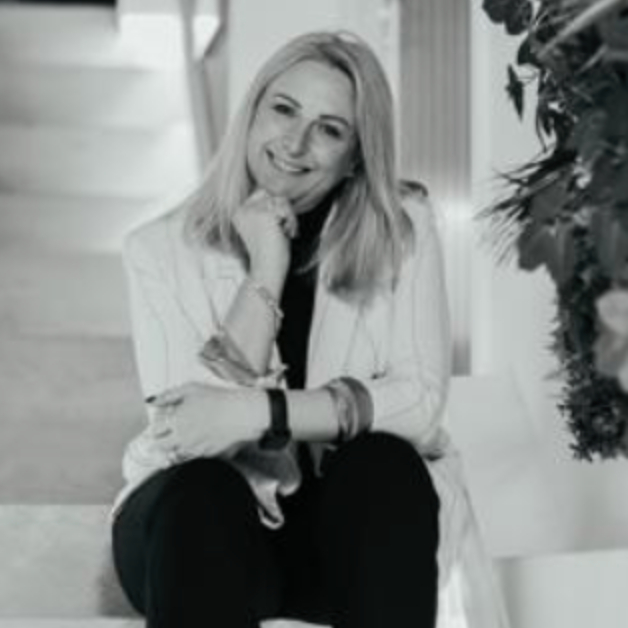 female with mid length blond hair wearing trousers and jackets sat on stairs