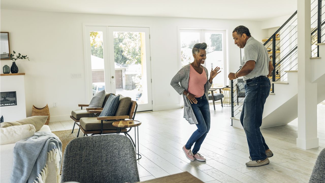 A happy retired couple dance in their living room.