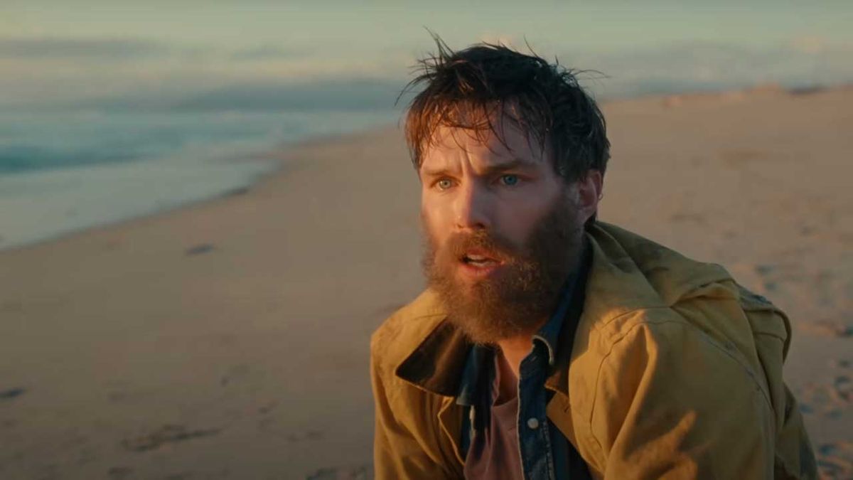 A bearded Nicholas Hoult on a beach