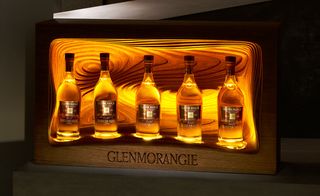 Glenmorangie winning design, five whisky bottles in a wooden display case with lights behind the bottles to highlight, grey floor and background