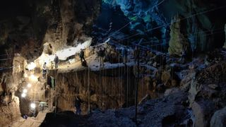 We see the inside of a dark cave filled with ropes and lights for an excavation.