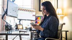 Day trader woman working from home, sitting in front of computers and looking at her phone