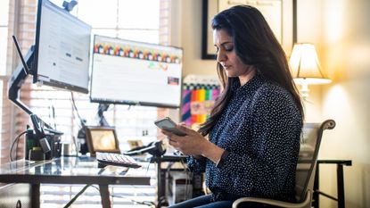 Day trader woman working from home, sitting in front of computers and looking at her phone
