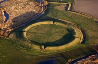 An aerial view of a giant ring fort (earth raised in a donut-like ring) in the countryside.