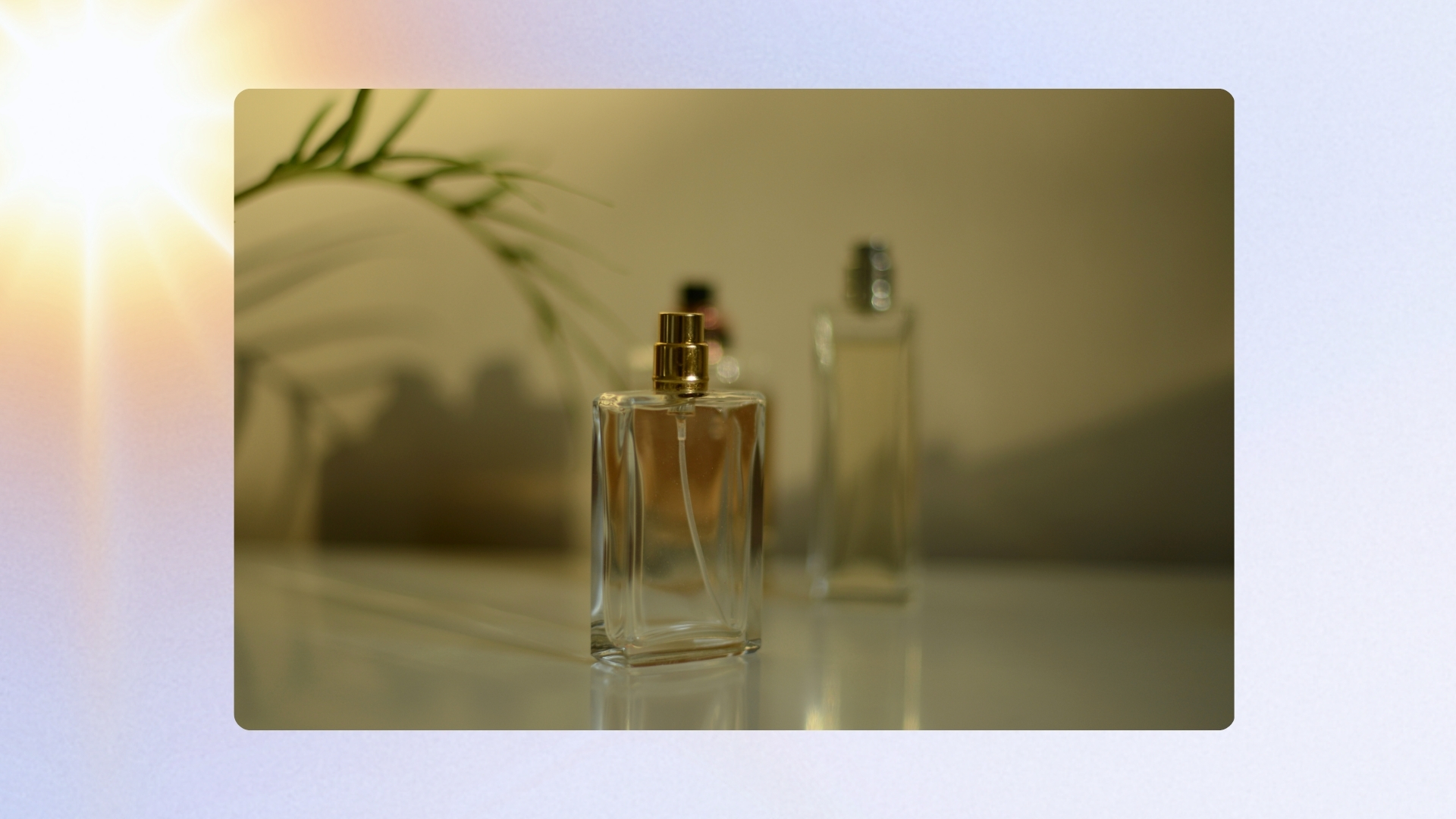A stock image of three glass perfume bottles sitting on a dresser in sunlight/ in a blue template with a yellow and pink sun effect.