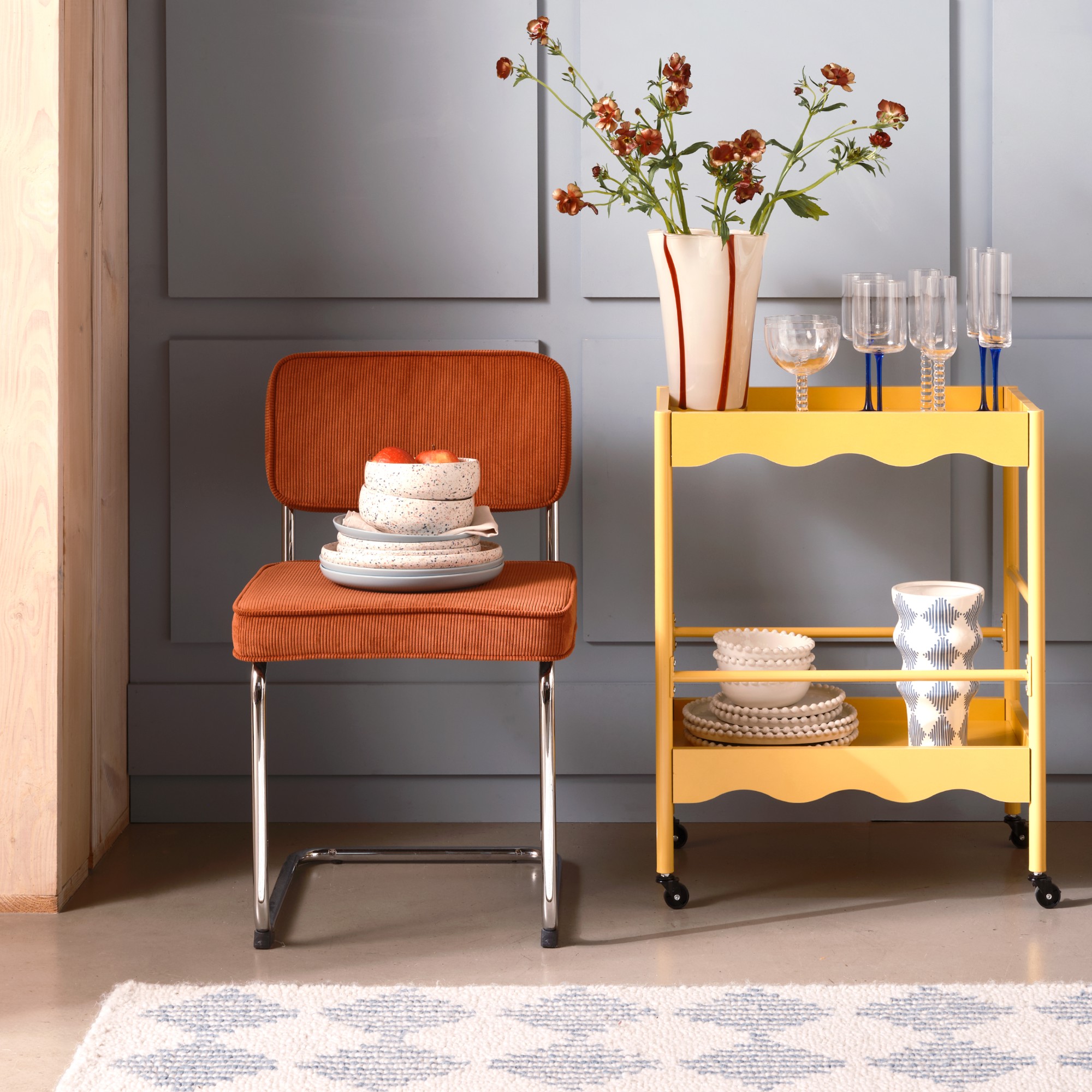 A chrome dining chair in rust cord with a scalloped yellow drinks trolley next to it