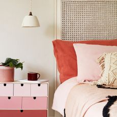A bed with coral pink bedding and a coral pink storage unit next to it