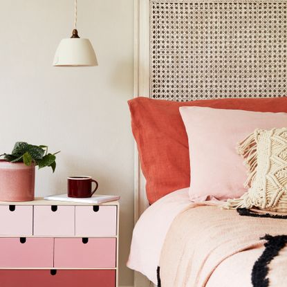A bed with coral pink bedding and a coral pink storage unit next to it