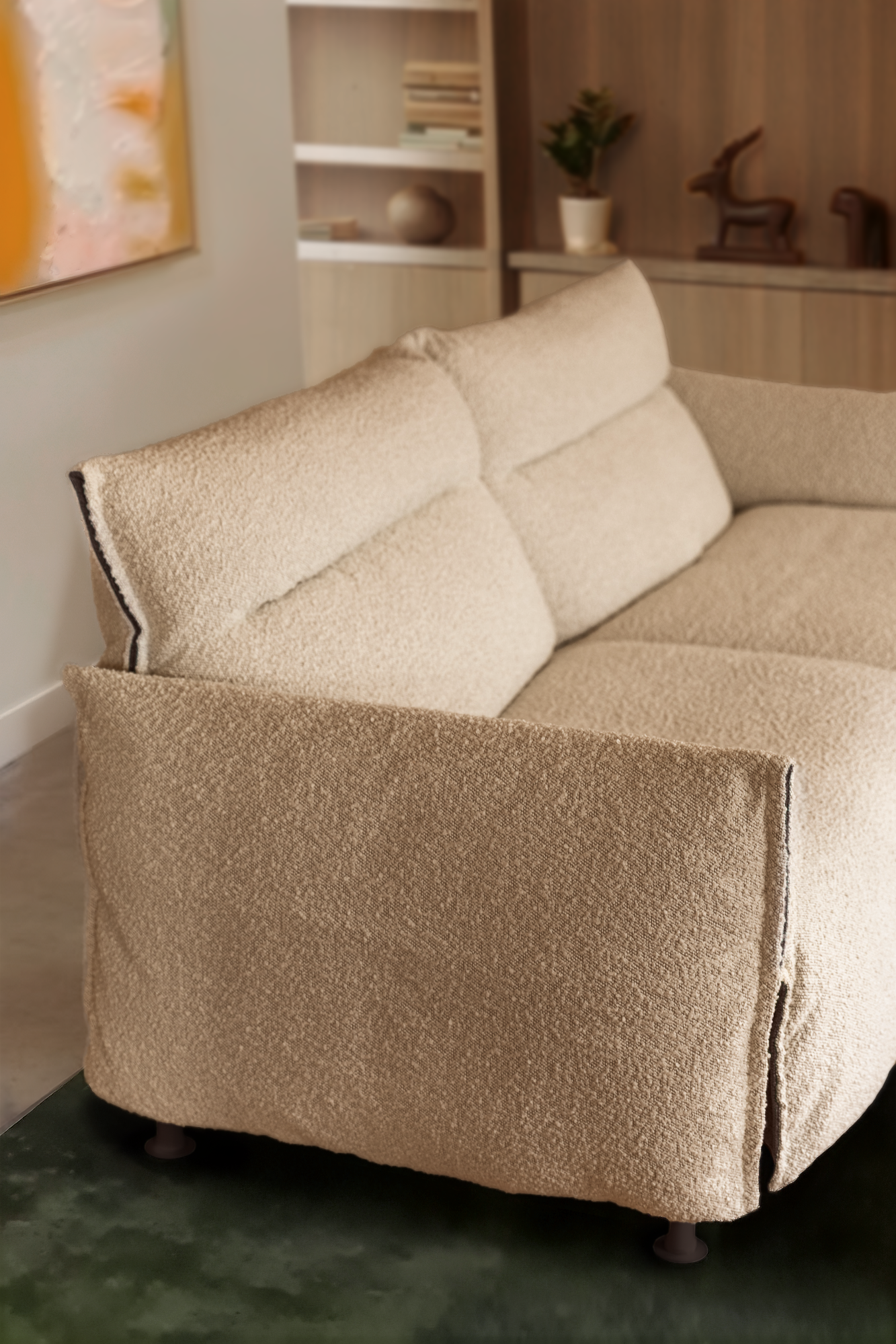 Close-up image of a white boucle sofa cover on a two-seater sofa. There is a green rug underneath and a wooden bookcase in the background.