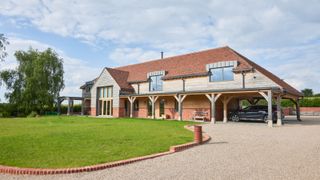 large oak frame home with sweeping gravel driveway surrounding lawned area with brick edging