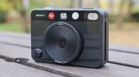 Front of a Leica Sofort 2 hybrid camera stood up on a slatted wooden table