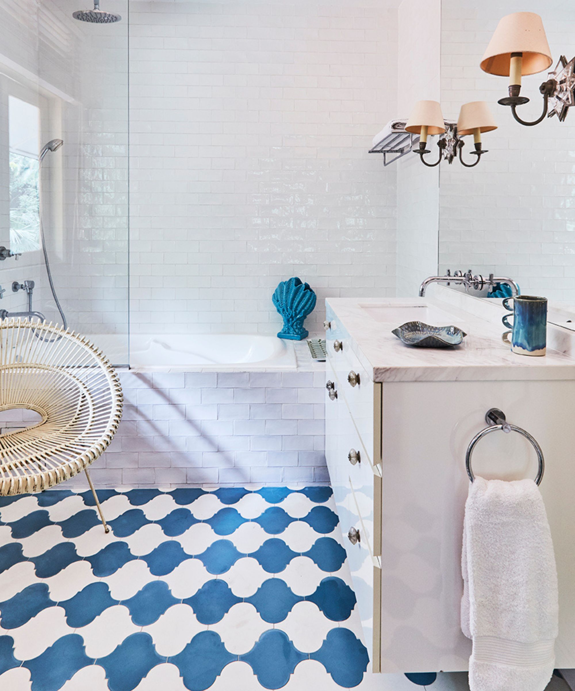 A white tiled bathroom with blue and white tiled flooring, a tiled bathtub, and a white cabinet with a white marble countertop and large mirror.