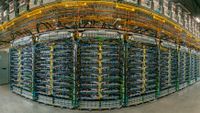 Rows of Google Ironwood TPU racks in a data center, with blue, green and yellow cabling under orange overhead cable trays.