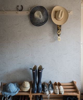 Subtle pale gray wallpaper ideas in a boot room, with a shoe rack and wall hooks with hats on.