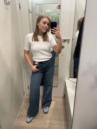 Woman in dressing room wears white t-shirt, blue jeans and blue trainers