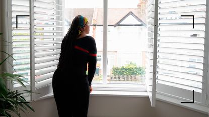 Woman opening bedroom shutters and looking out of the window to see daylight, one of the ways to learn how to wake up early