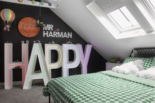 Kid's room with black painted feature wall and huge neon lettering spelling out 'HAPPY; black metal bed with green and white geometric bedding