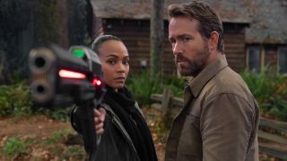 Zoe Saldana aims a big gun while Ryan Reynolds watches confused in The Adam Project.