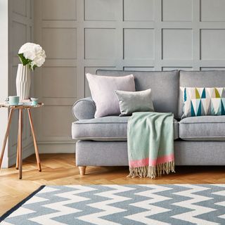 Grey sofa in living room with panelled wall and wooden floor