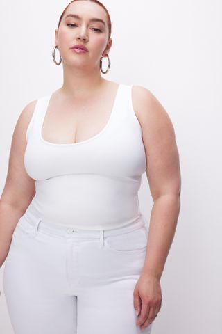 seorang model mengenakan tank top leher bulat putih dengan celana jins putih