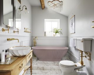A master bathroom with a freestanding pink tub, brass fittings and a chandelier