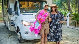 Alison and Aidan standing in front of a campervan while Aidan holds a bright pink donkey 