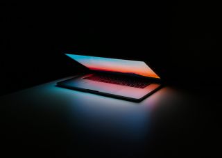 Partly open laptop computer glows colorfully in dark space