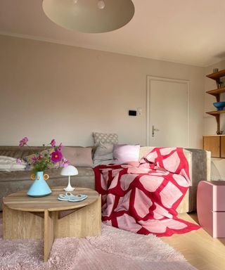 A living room with a pink and red throw on a brown couch and a circular coffee table