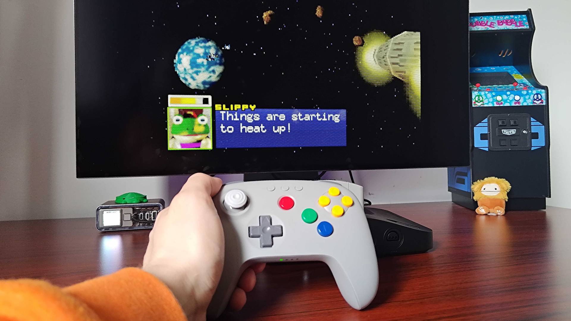 Hand holding 8bitdo N64 controller in front of Analogue 3D connected to LG OLED monitor with Slippy Toad on screen and text that reads "Things are starting to heat up!"