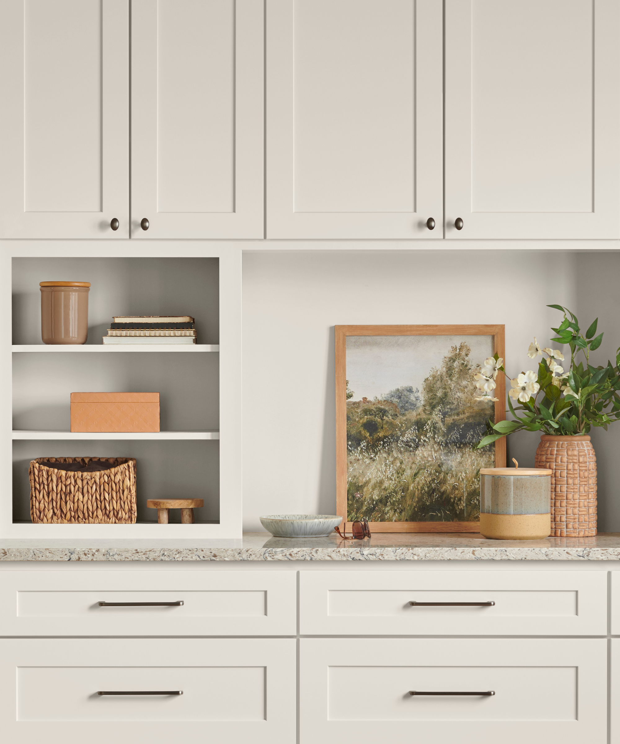 Beige kitchen cabinets with a framed painting and small decorations on the counter