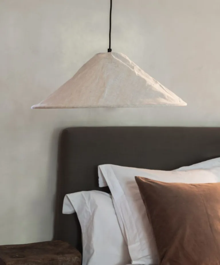 A brown bedframe with layered white and brown cushions in the background of a low hanging, light beige pendant light