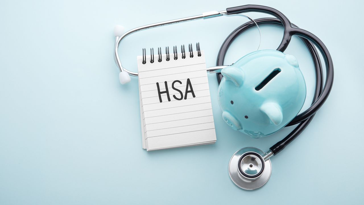 The letters HSA on a spiral notebook with a stethoscope and piggy bank against a blue background.