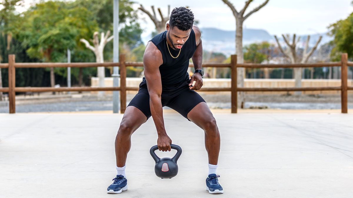 a photo of a man bending to pick up a kettlebell