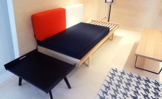 A wooden framed day bed with blue, red and black cushions.