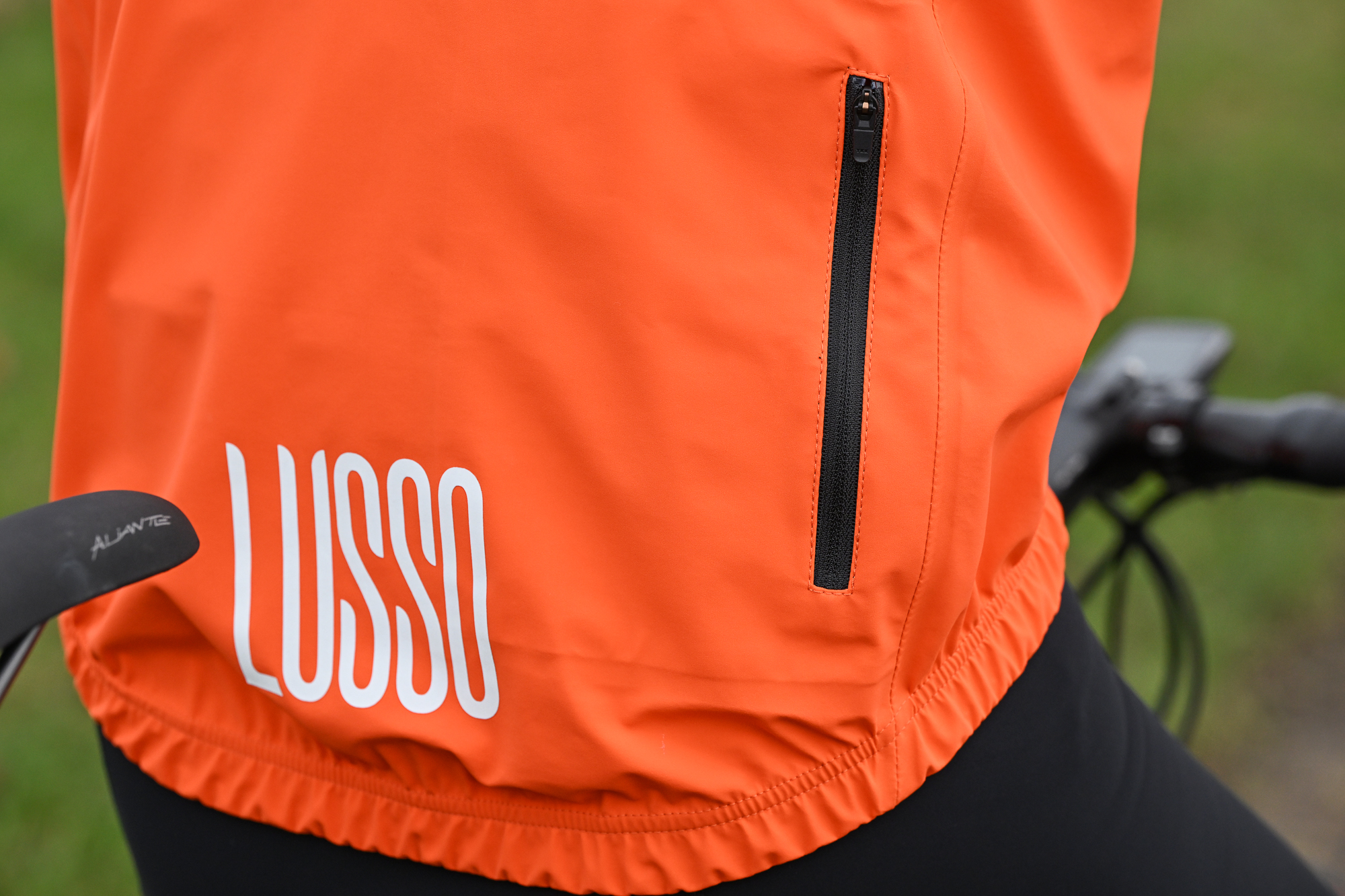 Close up of the rear of an orange jacket, showing the LUSSO branding and zipped pocket