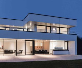 A contemporary white home with flat roof, a large terrace and extensive windows and doors from Internorm, shot at dusk with the lights on