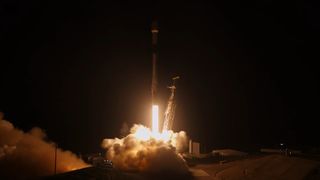 a white rocket lifts off in the dark early morning above a pillar of fire