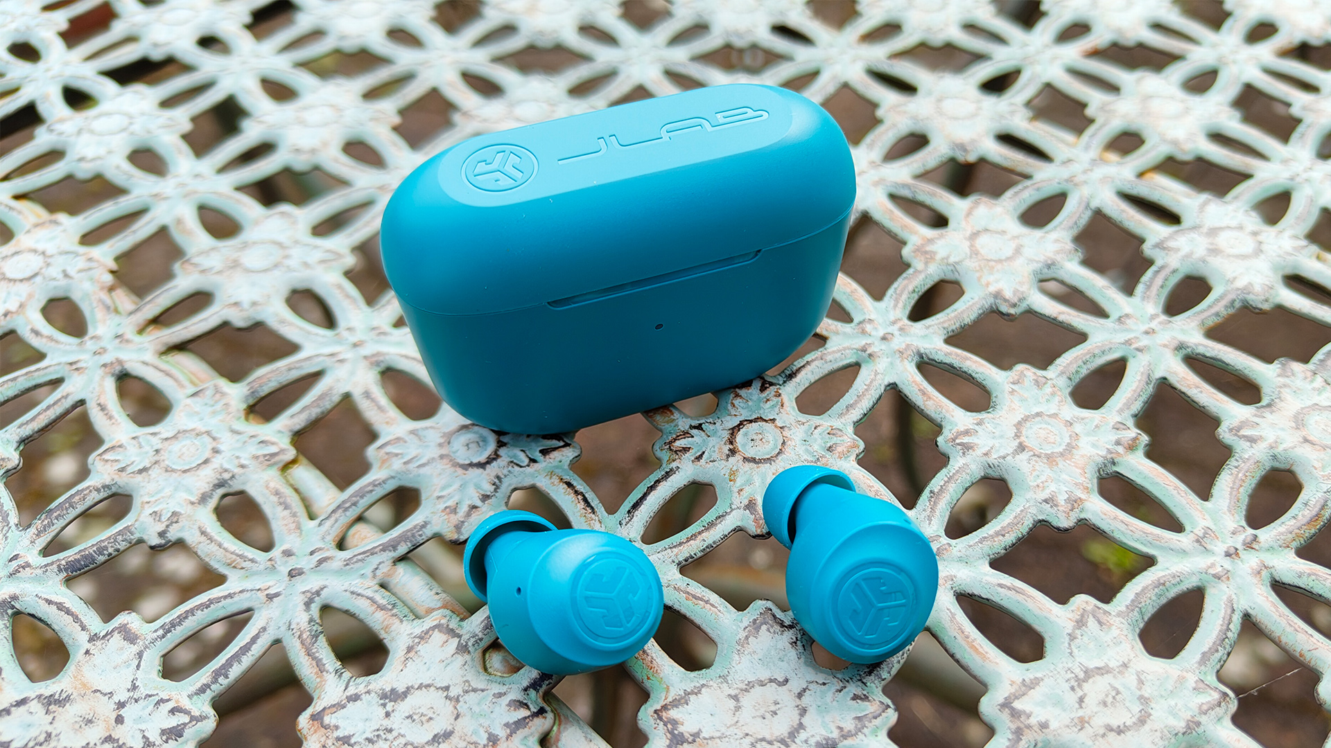 JLab Go Pop+ in-ear headphones on latticed garden furniture next to charging case